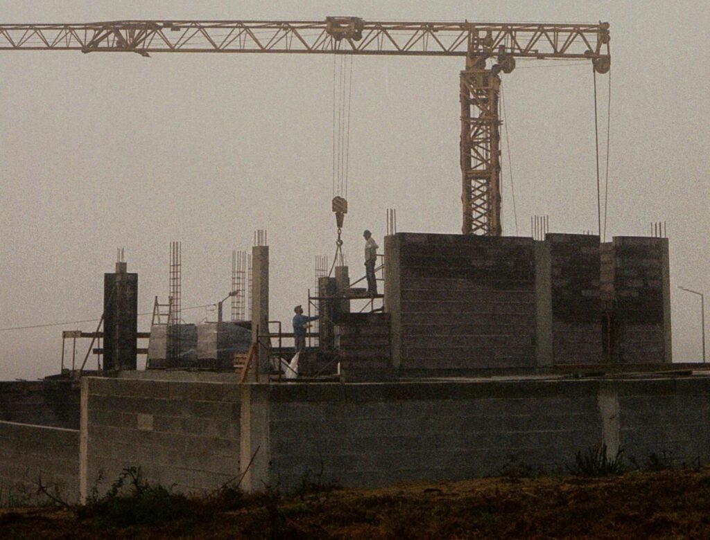 A misty, early morning view of a construction site with a crane and workers building amidst dense fog.